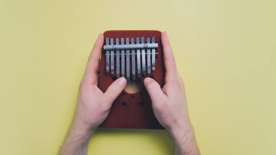 Hands Playing Small Kalimba Instrument on Yellow Background