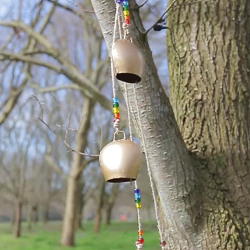 Handmade brass cowbell windchime with decorative bells hanging on a tree